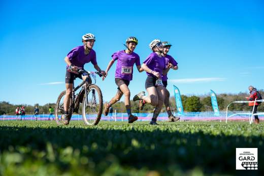Photo de 3 jeunes athlètes, 1 en VTT, les 2 autres en course à pied sur une pelouse bien verte et un ciel bleu azur